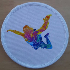 Könnte beinhalten: Ein weißer runder Patch mit einer bunten Silhouette eines Fallschirmspringers in der Luft. Der Fallschirmspringer ist in Gelb-, Orange-, Rosa-, Blau- und Grüntönen bemalt.