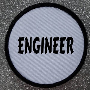 Op de afbeelding: Ronde witte patch met een zwarte rand en het woord "ENGINEER" in zwarte letters.