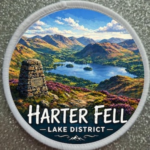 Könnte beinhalten: Ein runder Aufnäher mit einer Landschaft von Harter Fell im Lake District. Das Bild zeigt einen See, umgeben von Bergen, mit einem Steinmarker im Vordergrund. Der Text auf dem Aufnäher lautet "Harter Fell - Lake District".