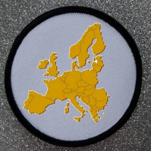 Puede incluir: Un parche circular blanco con borde negro, que presenta un contorno dorado del mapa de Europa.