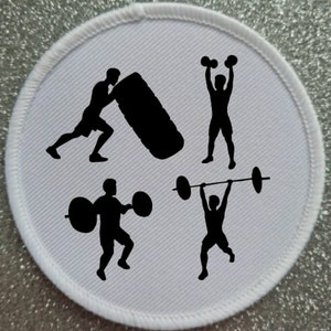 May include: A white round patch with black silhouettes of four people exercising. One person is lifting weights, another is lifting a barbell, another is pushing a tyre, and the last person is lifting dumbbells.