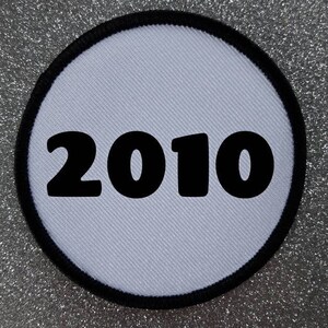 Op de afbeelding: Ronde witte patch met een zwarte rand en het jaar 2010 in het zwart gedrukt.