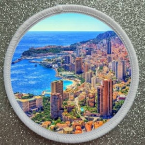 Könnte beinhalten: Eine farbenfrohe Luftaufnahme einer Stadt mit Gebäuden und einem blauen Meer. Die Stadt ist an einem Hang gebaut und hat viele hohe Gebäude. Das Meer ist leuchtend blau und es gibt weiße Boote im Wasser.