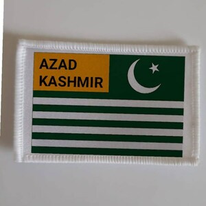 Op de afbeelding: Een witte patch met groene en gele randen. De patch heeft de tekst "AZAD KASHMIR" in zwarte letters en een witte halve maan met een witte ster erin op een groene achtergrond.