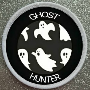 May include: A white round patch with black text and white ghost silhouettes. The text reads "Ghost Hunter".