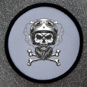 May include: A white embroidered patch featuring a black skull wearing a motorcycle helmet and goggles. The skull has a beard and is surrounded by smoke. Two crossed bones are below the skull.