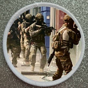 May include: A group of soldiers in camouflage gear are shown in an urban setting. They are holding rifles and appear to be on a mission. The soldiers are wearing helmets and tactical vests. The image is a close-up of the soldiers and their weapons.