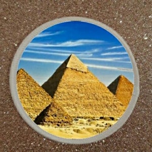 May include: A close-up view of three large, ancient pyramids in the desert. The pyramids are made of light brown stone and are set against a bright blue sky with white clouds.