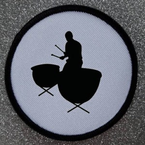 May include: A white circular patch with a black outline featuring a silhouette of a person playing a pair of timpani drums.