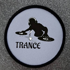 Op de afbeelding: Een witte ronde patch met een zwarte rand toont een silhouet van een DJ die muziek mixt op twee draaitafels. De tekst "TRANCE" is in zwart onder de DJ gedrukt.