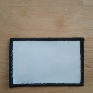 Könnte beinhalten: Ein weißer, leerer Patch mit einem schwarzen, gestickten Rand. Der Patch ist aus Stoff und kann individuell gestaltet werden.