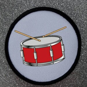 May include: A red and silver drum with two wooden drumsticks. The drum is on a white background with a black border.