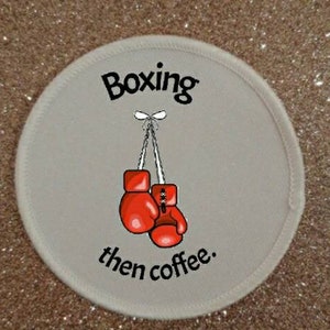 Può includere: Un cerotto rotondo bianco con il testo "Boxing then coffee." Due guantoni da boxe rossi sono appesi al testo.