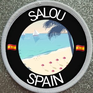 May include: A round, white-bordered patch with a black background. The patch features a beach scene with palm trees, sailboats, and pink umbrellas. The text "SALOU" and "SPAIN" are written in white on the patch, along with two small Spanish flags.