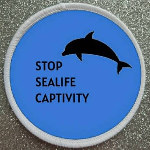 May include: A white circular patch with a blue background and a black silhouette of a dolphin jumping out of the water. The text "STOP SEALIFE CAPTIVITY" is printed in black letters.