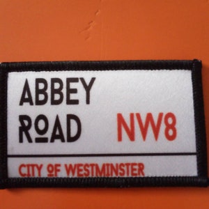 May include: A white patch with black trim and red text that reads "Abbey Road NW8 City of Westminster".