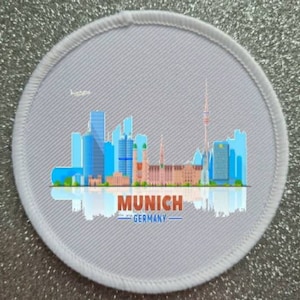Peut inclure: Patch rond blanc avec un fond gris et une illustration colorée de l'horizon de Munich. Le texte "MUNICH - GERMANY" est imprimé sous l'horizon.