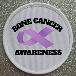 May include: White round patch with a purple ribbon and the text "Bone Cancer Awareness" in black.