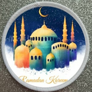 May include: A white round patch with a blue background and a crescent moon in the top left corner. The patch features a watercolour illustration of a mosque with multiple domes and minarets. The text "Ramadan Kareem" is written in gold script at the bottom of the patch.