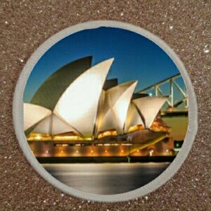May include: A nighttime view of the Sydney Opera House, a famous architectural landmark in Australia. The building is illuminated with warm white lights, and the water surrounding it is calm and reflective. The sky is a deep blue, and there are a few stars visible.