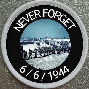 Può includere: Una toppa circolare in bianco e nero con testo bianco che recita "NEVER FORGET 6/6/1944". Il centro della toppa presenta una fotografia in bianco e nero di soldati che camminano su una spiaggia.