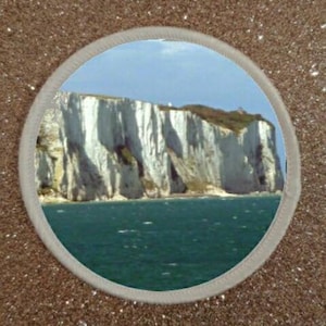 May include: A scenic view of white cliffs rising from the ocean. The cliffs are tall and jagged, with a blue sky above. The water is a deep blue, and there are whitecaps on the waves.