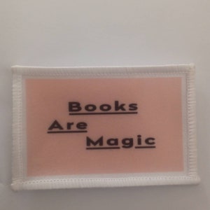 May include: A white fabric patch with a pink background and black text that reads "Books Are Magic".