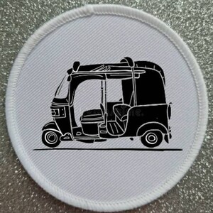 Op de afbeelding: Een zwart-witte illustratie van een driewielige auto-riksja, ook wel tuk-tuk genoemd, op een witte achtergrond.