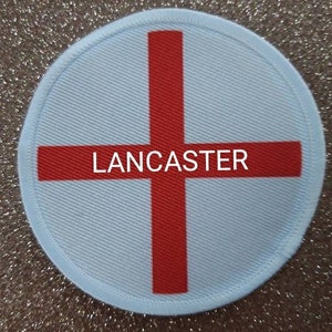 May include: A white round patch with a red cross and the word "LANCASTER" in the center.