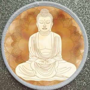 Puede incluir: Una estatua blanca de Buda meditando en posición de loto sobre un fondo de mandala amarillo y naranja.