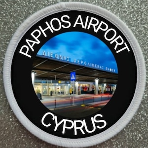 May include: A white and black circular patch with the text "Paphos Airport Cyprus" and a photo of the airport terminal building in the center.