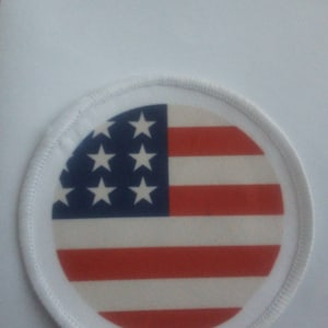 Op de afbeelding: Een witte ronde patch met een rood, wit en blauw Amerikaans vlagontwerp.