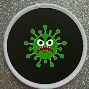 May include: A round black patch with a white border features a green cartoon virus with an angry face. The virus has a red mouth and white eyes.