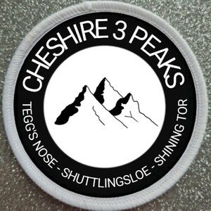 Puede incluir: Parche redondo blanco y negro con el texto "Cheshire 3 Peaks" y "Tegg's Nose - Shuttlingsloe - Shining Tor" alrededor de un círculo negro con una imagen estilizada de tres picos de montaña en su interior.
