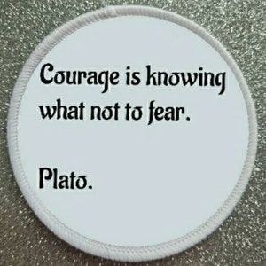 Puede incluir: Parche redondo blanco con texto negro que dice "El coraje es saber qué no temer. Platón."