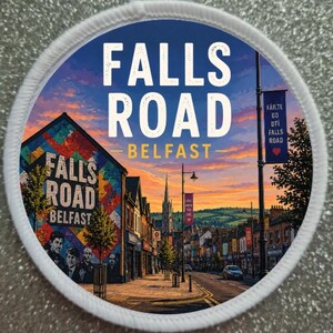 May include: A round patch with a detailed illustration of Falls Road in Belfast, Northern Ireland. The patch features the text "FALLS ROAD BELFAST" in white, set against a vibrant sunset sky and a colorful mural.