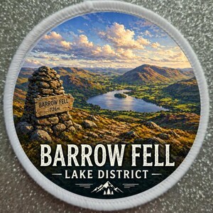 May include: Circular patch depicting Barrow Fell in the Lake District. The image shows a lake, hills, and a sign reading "BARROW FELL 726m". The text "LAKE DISTRICT" is also present, with a mountain graphic below.