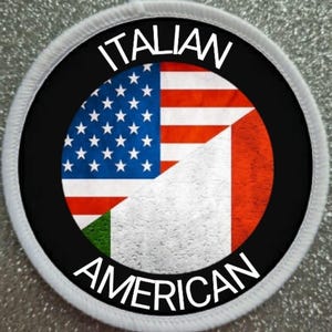 Może przedstawiać: Biała okrągła łatka z czarnym okręgiem w środku. Czarny okrąg zawiera napis "ITALIAN AMERICAN" białymi literami wokół krawędzi. Wewnątrz czarnego okręgu znajduje się połowa flagi amerykańskiej i połowa flagi włoskiej.