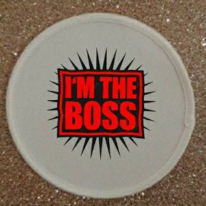 May include: White round patch with a black starburst design. The centre of the patch has a red square with the text "I'M THE BOSS" in black.