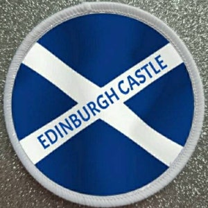 May include: A round patch featuring the Scottish flag design, a blue background with a white diagonal cross. The text "EDINBURGH CASTLE" is printed in white across the center. The patch has a white border.