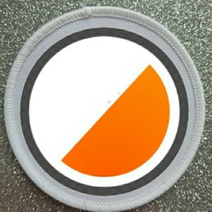 May include: A white and orange round patch with a grey border. The orange section is a half circle.