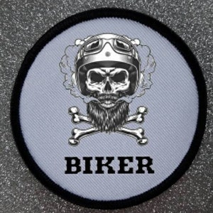 Może przedstawiać: Okrągła, biała łatka z czarną obwódką. Łatka przedstawia czaszkę w kasku motocyklowym i okularach, z brodą i skrzyżowanymi kośćmi. Słowo "BIKER" jest nadrukowane czarnym kolorem pod czaszką.