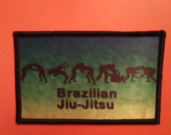 May include: A rectangular patch with a black border and a green and blue gradient background. Silhouetted figures demonstrate Brazilian Jiu-Jitsu moves above the words "Brazilian Jiu-Jitsu" in white.