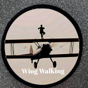 May include: A black and white photograph of a biplane with a person wing walking. The text "Wing Walking" is printed below the plane.
