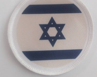 May include: A white circular patch with a blue Star of David and two blue horizontal stripes. The patch has a white stitched border.