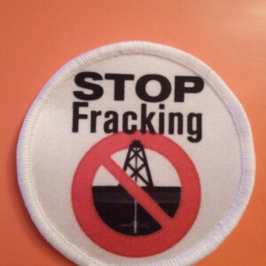 May include: White round patch with a red circle and a black oil rig with a diagonal red line through it. The text "STOP Fracking" is printed in black letters.