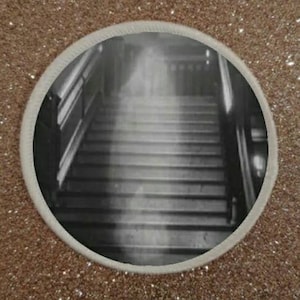 Può includere: Una fotografia in bianco e nero di una scala con una figura spettrale che sembra fluttuare verso il basso lungo i gradini.