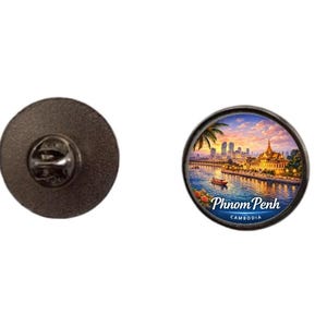 May include: A round pin with a detailed image of Phnom Penh, Cambodia, featuring a river scene with buildings and the text "Phnom Penh Cambodia". The pin has a black border and a pin back.