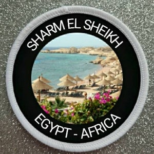 Pode incluir: Um remendo redondo branco e preto com o texto "SHARM EL SHEIKH EGYPT - AFRICA" e uma foto de uma cena de praia com palmeiras e guarda-sóis.