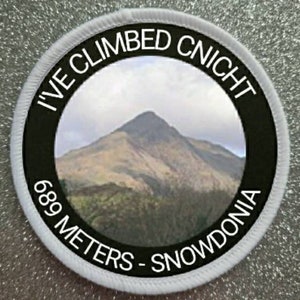 Puede incluir: Parche redondo blanco con texto negro y una foto de una montaña. El texto dice "I've Climbed Cnicht 689 Metros - Snowdonia".